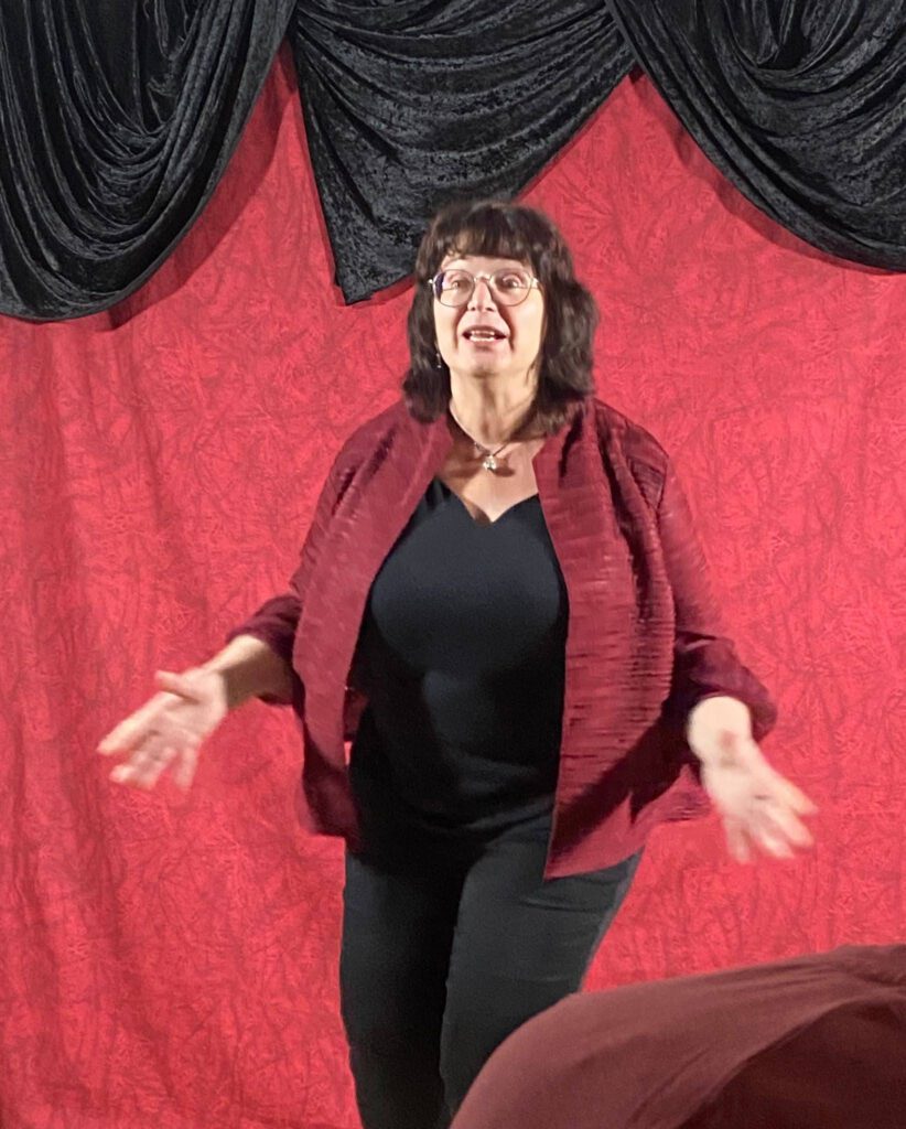 Erzählerin Christine Graf bei einer Gruselgeschichte in Tittling und Tiefenbach; im passenden schwarz-roten Outfit vor düsterem Hintergrund.